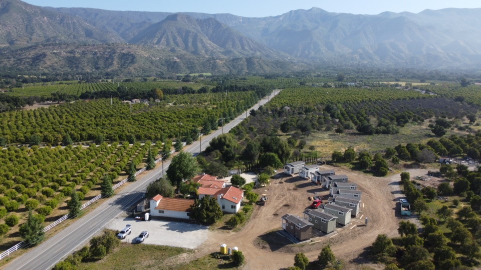 Aerial view of farmland, road, and houses with mountains in the background.