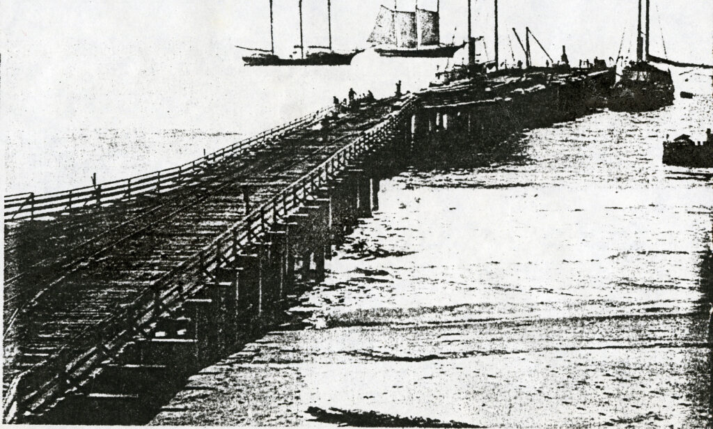 Historical black and white photo of original Hueneme Wharf, showcasing old dock and ships.