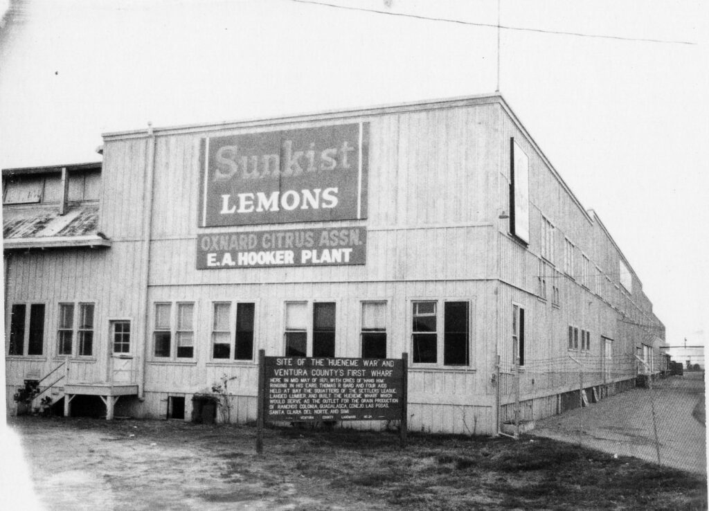Historical black and white photo of the original Hueneme Wharf site with signage.