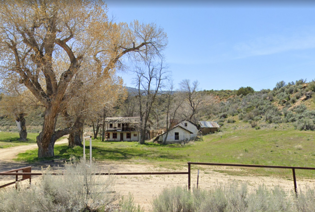 View of adobe ruins surrounded by mature trees and hills, April 2023.
