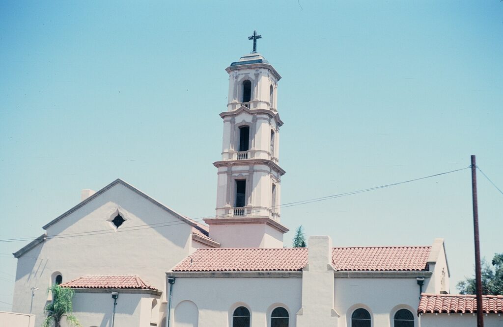 St. Mary Magdalen Church featuring a tall bell tower, Spanish Neo-Classic architecture, red tile roof, and white stucco walls, 1978.